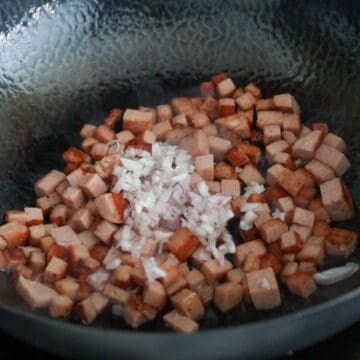 Diced Spam frying in a hot wok until golden brown, with shallots being added and cooked until soft and lightly caramelised.