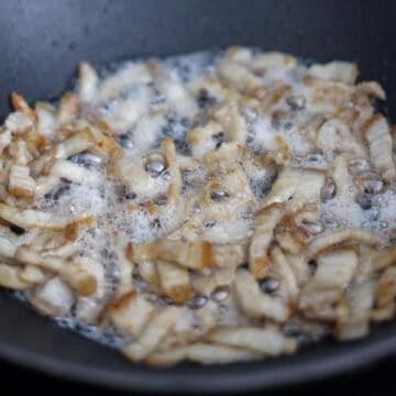 Cooking sliced pork belly in a pan until browned with rendered fat remaining in the pan