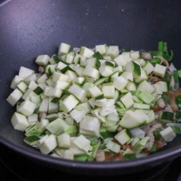 Sautéing onions and green onions until softened, then cooking zucchini and cabbage until tender