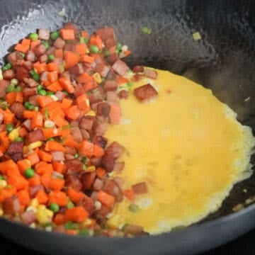 Beaten eggs poured into an empty space in a hot wok, gently setting before being scrambled into soft, bite-sized pieces.