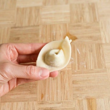 Lightly dab water onto one of the triangular tips. Bring the two tips together and pinch it together to create a wonton. Transfer wrapped wontons to a large baking sheet or a large plate lined with parchment paper to prevent them from sticking to the surface.