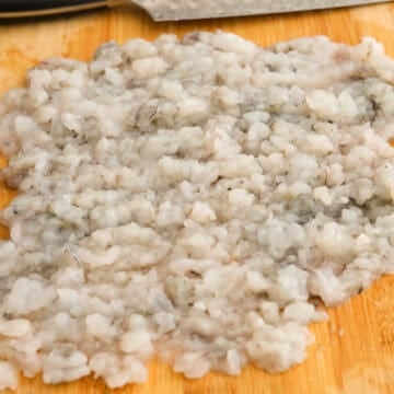 Finely chop peeled and deveined shrimp with a knife into a fine sticky paste. Transfer finely chopped shrimp to a large mixing bowl.