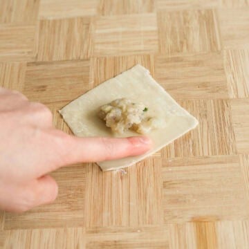 Spoon 1 levelled teaspoon of the filling into the center of a wonton wrapper. Prepare a small bowl of cold water nearby and lightly dab a bit of water on two adjacent edges of the wrapper.