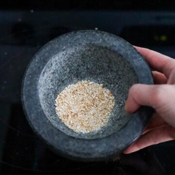 Rice grains toasting in a dry pan.
Toasted rice being ground into a fine powder.