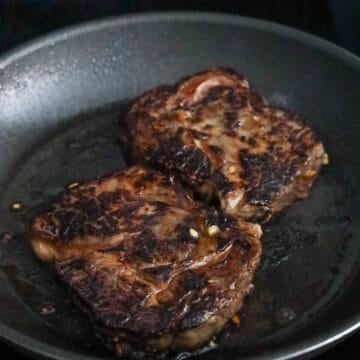 Steaks searing in a hot cast-iron skillet.