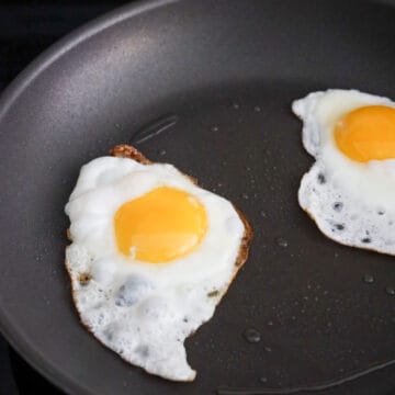 Eggs frying sunny-side up in a pan with set whites and runny yolks.