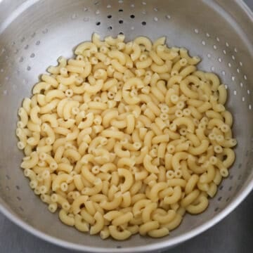 Cooked pasta being drained in a colander and divided into two large bowls.