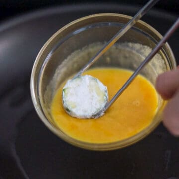 Heat 1 tablespoon or 15 ml of vegetable oil in a large pan on medium heat. Then dip a zucchini slice into the egg batter and lower it into the pan. Repeat this until three-quarters of the pan is filled and do not over crowd. You'll need to fry in batches.