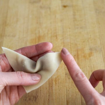 Fold the wonton into a triangle shape so the opposite corner is sealed to the other one. Push out any air bubbles and seal the edges of the wrapper. Dab water on the bottom left or right tip of the triangle. 