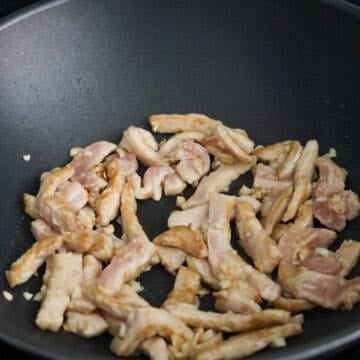 Then in a large wok or large skillet on medium high heat, add vegetable oil. Once oil is hot, add garlic and marinated pork. Fry until pork is about 75% cooked.