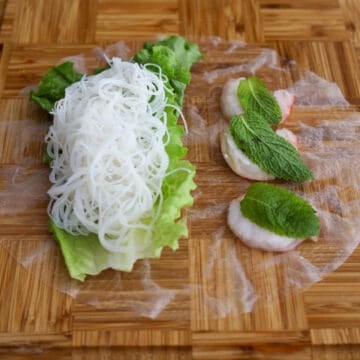 Place a piece of lettuce in the bottom half of the circular wrapper. Then place 3 shrimp halves pink side down in the top half of the circular wrapper. Place mint leaves on top of each shrimp. Lastly with wet hands, place about ⅓ cup of cooked vermicelli rice noodles inside the lettuce leaf and spread it into a log.