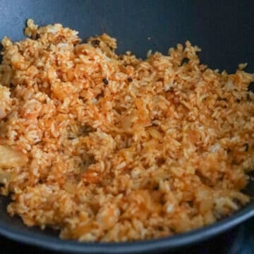 Add in day-old cooked rice, kimchi juice, gochujang, sesame oil and toss everything together until rice are colored red.