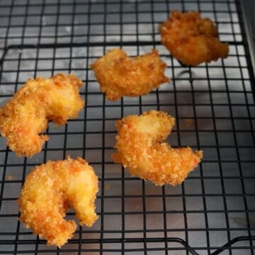 Fried shrimp draining on a wire rack or paper towel-lined plate to remove excess oil.