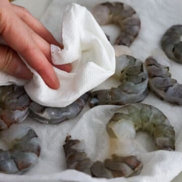 Raw jumbo shrimp being peeled, deveined, and patted dry with paper towels before breading.