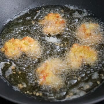 Breaded shrimp frying in hot oil in a pan until golden brown and crisp, with small batches cooking at once.