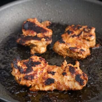 Marinated chicken thighs being pan-fried in a skillet over medium heat until cooked through with lightly charred edges.