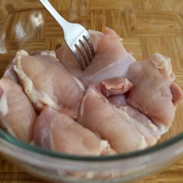 Chicken thighs being pierced with a fork and placed into a large bowl or zip-top bag for marinating preparation.