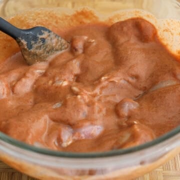 Chicken thighs being fully coated in marinade inside a covered bowl or sealed bag and refrigerated to marinate.
