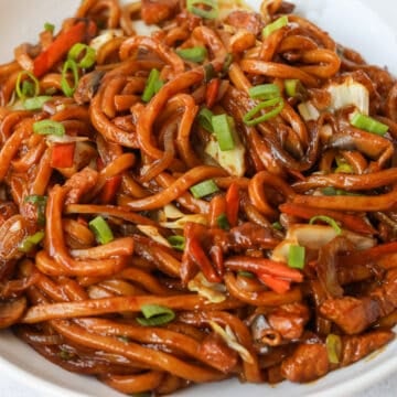 Cooked noodles transferred to a serving plate and garnished with chopped green onions.