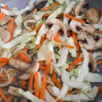 Garlic and onions stir-frying in a pan, followed by cabbage, mushrooms, and carrots until tender.
