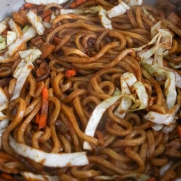 Noodles, sauce, and cooked pork belly being tossed together in a pan until evenly coated.