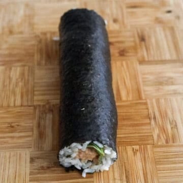 Begin rolling the kimbap by starting at the end closest to you. Firmly roll and tuck the ingredients and be careful not to squeeze the tuna filling out as you roll. Once you reach the end, let the roll sit on top where the border was so it can stick to the rest of the roll with the residual heat from the rice.