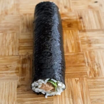 Then evenly pour ½ teaspoon sesame oil on the kimbap roll and with clean hands or a brush, spread it all over the seaweed. Repeat the above steps for the remaining roll.
