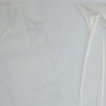 Next spread out a large fresh sheet of plastic wrap or cling film (about 15 x 15 inches) on a clean surface where the plastic will cling to (like a large ceramic plate or on a countertop with the corners taped down). Moisten the rice paddle or a silicone spatula with water and divide cooked rice into four equal portions.