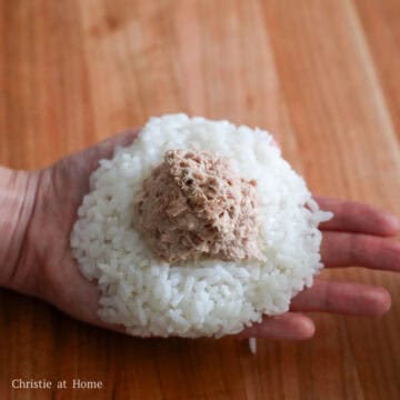 Prepare a bowl of water nearby and dip clean hands into the water. Take ½ cup or 100 grams cooked rice and place it into the palm of your hand. Shape it into a round ball, then flatten into a ½-inch thick pancake. Make a dent in the middle. Place 2 tablespoon or 30 ml of tuna mayo mixture into the dent.(If you have an onigiri mold or a large sheet of plastic wrap, use these tools to help easily mold the rice balls to prevent a sticky mess)