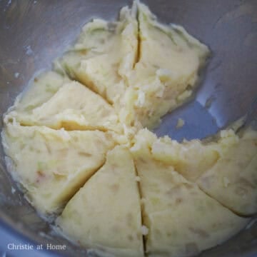 Mashed potato and onion mixture being gently combined in a bowl with seasonings.