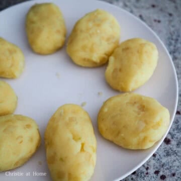 Oval-shaped potato croquettes being formed by hand and placed on a tray.