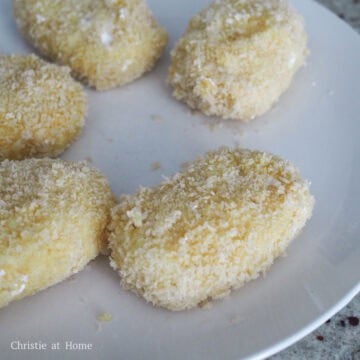 Potato balls being coated in cornstarch, egg, and panko breadcrumbs in separate dredging stations.
