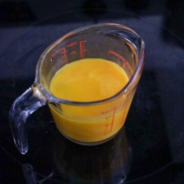 A small bowl with eggs being whisked until smooth, next to a measuring cup with a spout.