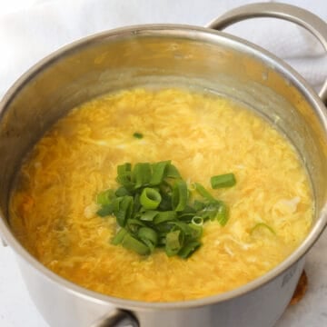 Eggs being poured in a thin stream into simmering soup, forming thin egg ribbons. Finished egg drop soup in a bowl, garnished with chopped scallion greens, ready to serve.
