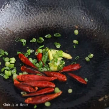 Ginger, red chilies, and green onions sautéing in a pan until fragrant.