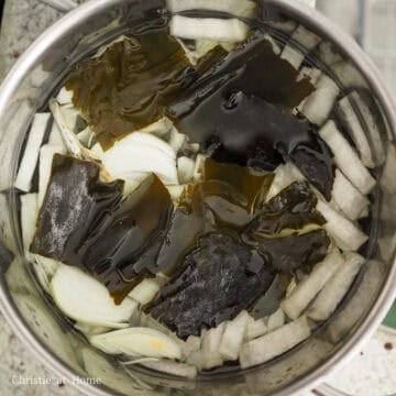 Ingredients simmering in a pot with anchovy broth tablets, dried kelp, onion, and green onion to create a light, savory broth.