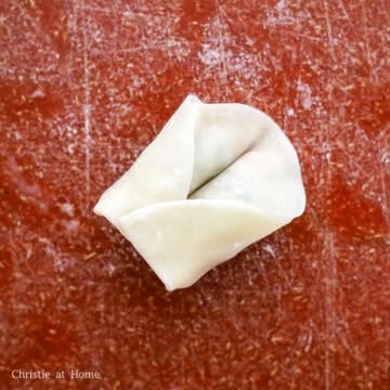Slightly push the middle of the folded wonton down with a chopstick. Then bring the ends together and pinch them together. Repeat this until you have no more filling or wonton wrappers left.