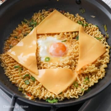 As soon as noodles are loosened, make a well in the center and crack an egg into it. Once the egg whites are opaque, add sliced cheese on top of the noodles and green onions.