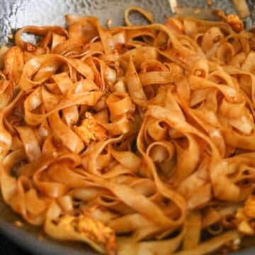 Add remaining vegetable oil into the empty space of the pan. Toss in rice noodles with noodle sauce mixing everything together. Taste test the noodles and if they are not al dente, add 2-4 tablespoons of water and cook until they become soft and chewy. If you're using a steel wok, let the noodles sit in the pan undisturbed so they can slightly char for a smoky flavor.