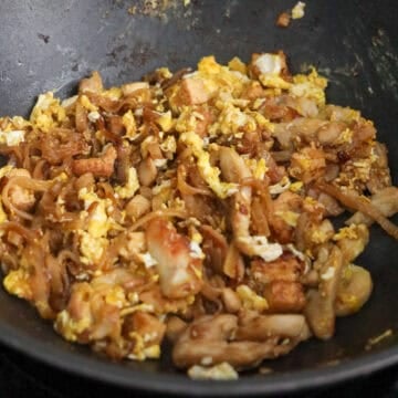 Mix in cooked chicken and push everything to the side of the pan. Add remaining oil into the empty space of the pan and add eggs. Scramble them first and then mix in with noodles.