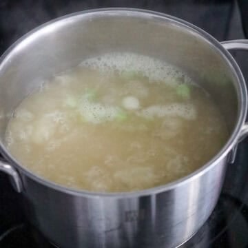 A medium pot on the stove with chicken stock and scallion whites heating to a boil.