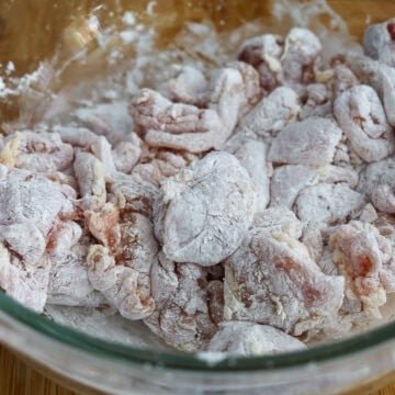 Chicken pieces in a large bowl being tossed with cornstarch until fully and evenly coated.