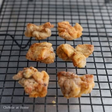 Fried chicken pieces resting on a wire rack or paper towel-lined plate as excess oil drips off.