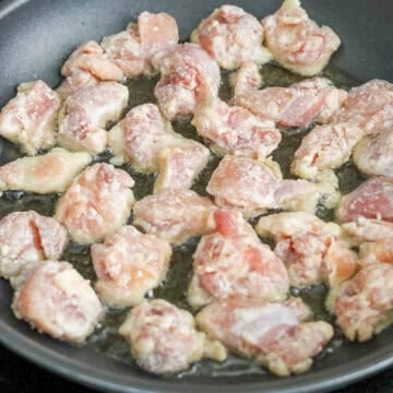 Chicken pieces frying in hot oil in a pan until golden and crispy on both sides.