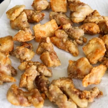 Fried chicken being transferred to a wire rack or paper towel-lined plate to drain excess oil.