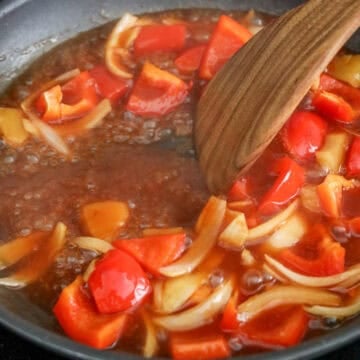 Chopped onions, red bell pepper, and pineapple sautéing in a pan, then sauce added and simmered until thickened.