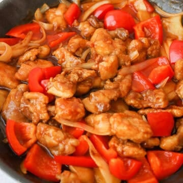 Fried chicken tossed in a thick, glossy sauce and garnished with green onions and sesame seeds before serving.
