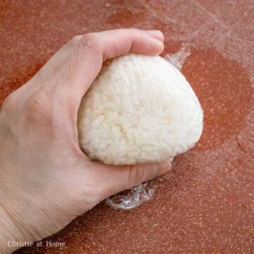On a clean working surface, spread out a large sheet of plastic wrap. Measure ½ cup of the seasoned rice and place it into the center of the plastic wrap. Wrap the rice into a ball and shape it into a triangle.