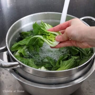 Slice baby bok choy into halves. Rinse the halved baby bok choy in cold water until it runs clear, and leaves are clean. Shake out as much excess water as possible. Set aside in the colander to continue straining.