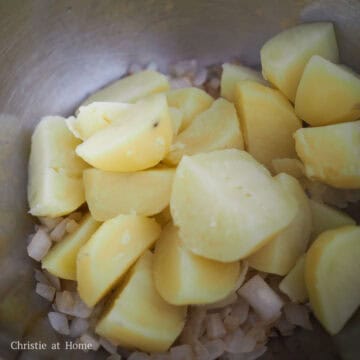 Sautéed onions being cooked in a pan before being mixed into mashed potatoes.